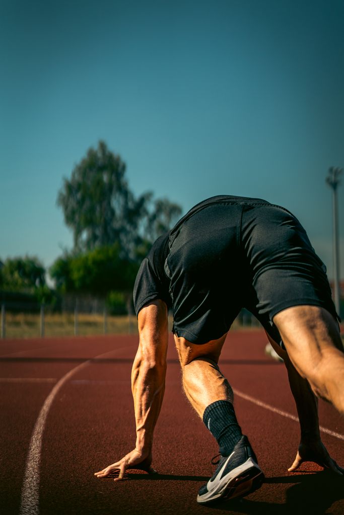 Athlete in a starting position on an outdoor running track under clear skies.